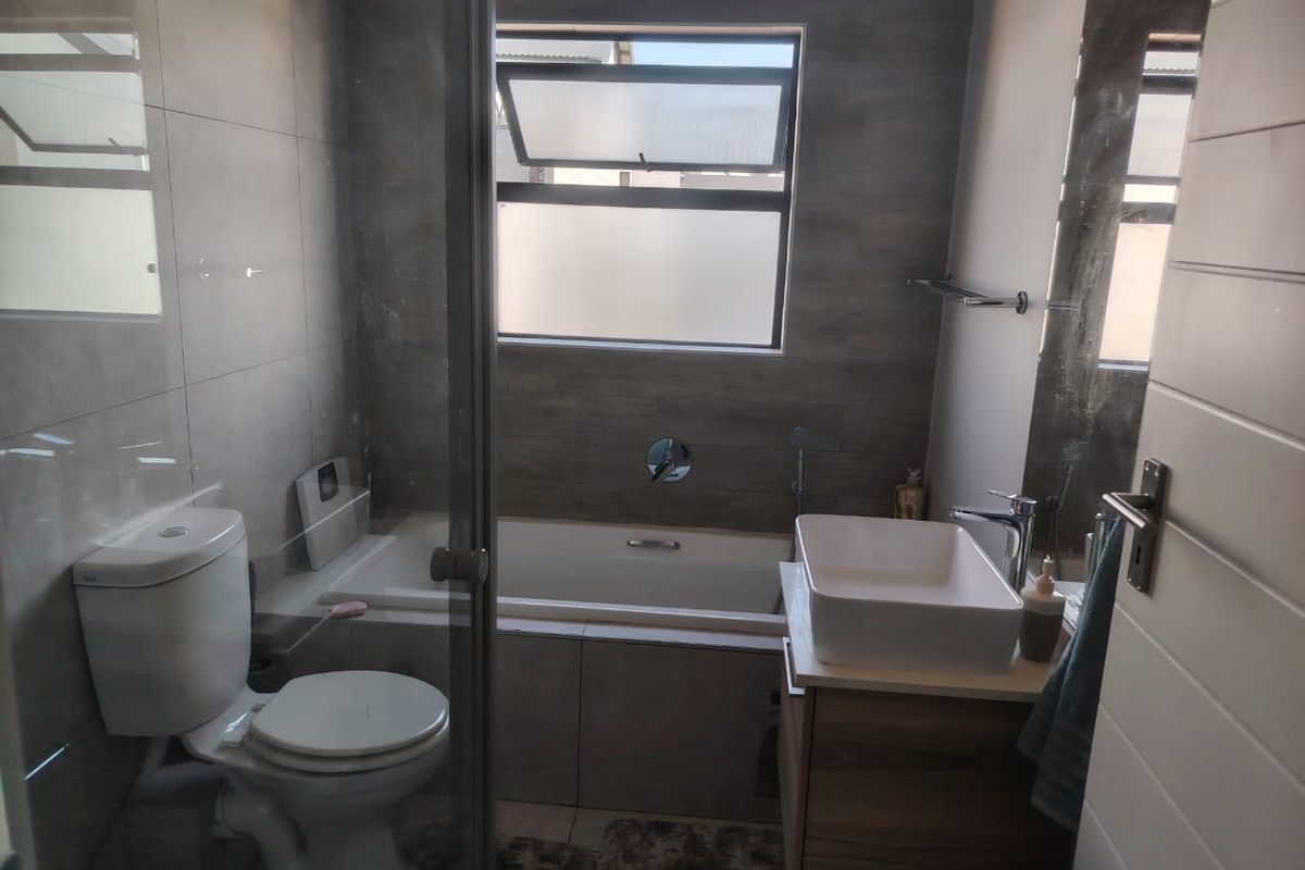 Modern bathroom featuring a built-in bathtub, glass shower enclosure, vessel sink vanity, and neutral grey wall tiling.