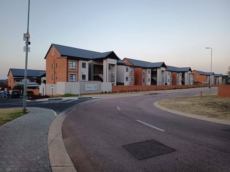 A street-level view of the Cherry Blossom townhouse complex, featuring multi-story brick and plaster residential buildings with pitched metal roofs.