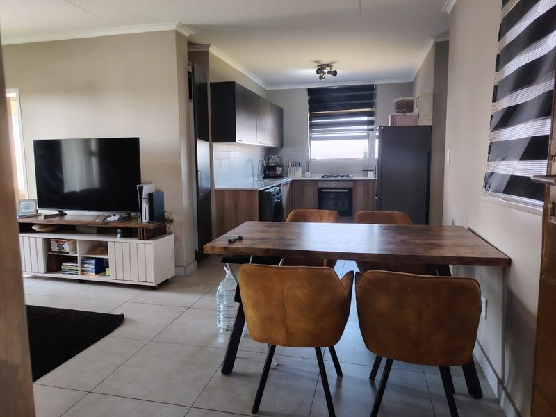 Open-plan living and dining area featuring a modern kitchen with built-in cabinetry, oven, and hob, complemented by neutral tiled flooring throughout.