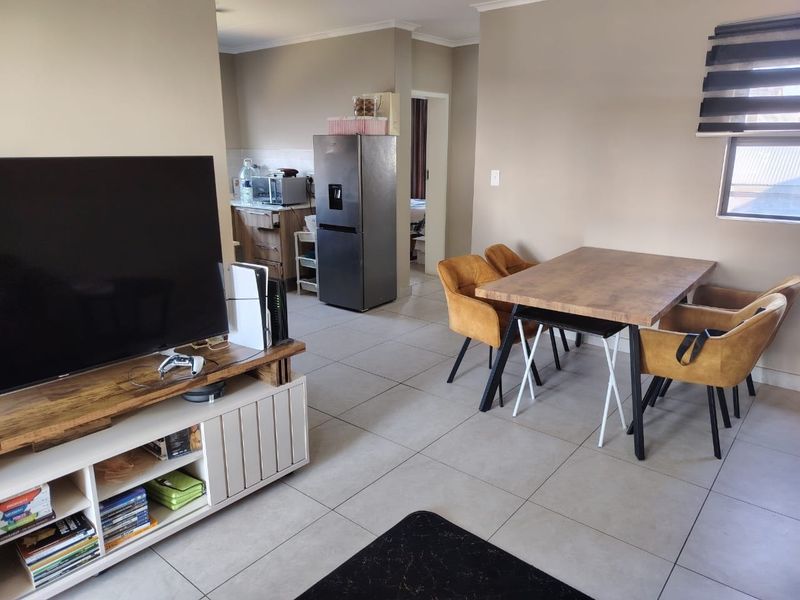 Open plan living and dining area featuring tiled flooring and neutral wall tones, with an adjacent kitchen space visible in the background.