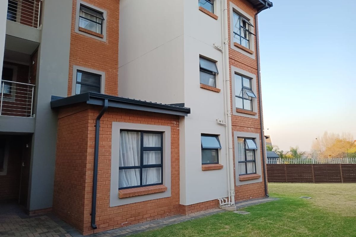 Rear view of a multi-story townhouse featuring a combination of brick and rendered facade, aluminium window frames, and a well-maintained lawn area.