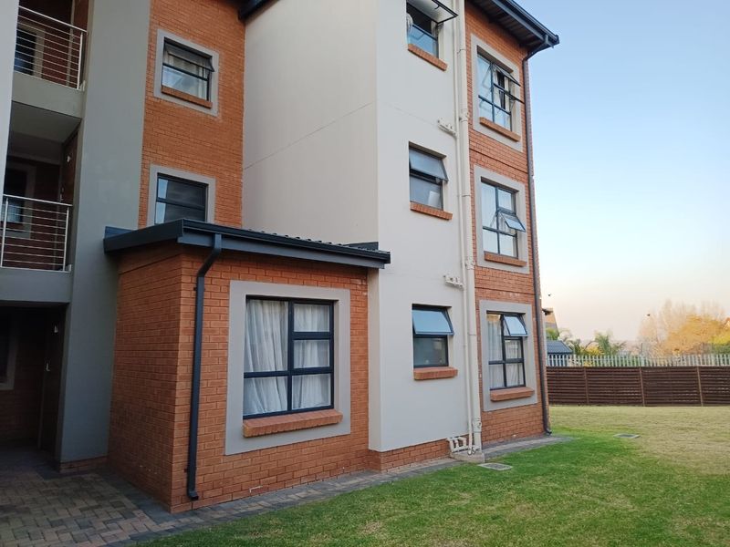 Rear view of a multi-story townhouse featuring a combination of brick and rendered facade, aluminium window frames, and a well-maintained lawn area.
