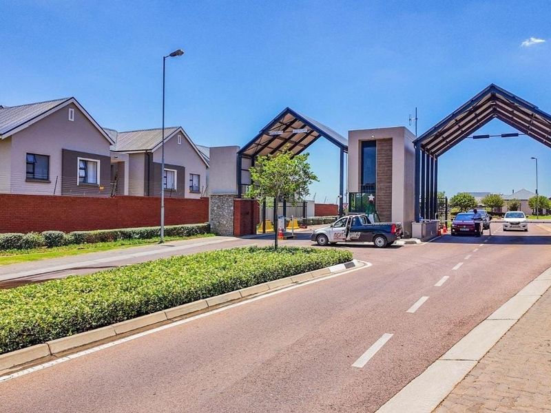 The entrance to the townhouse complex features a secure gatehouse, access control infrastructure, and well-maintained brick boundary walls.