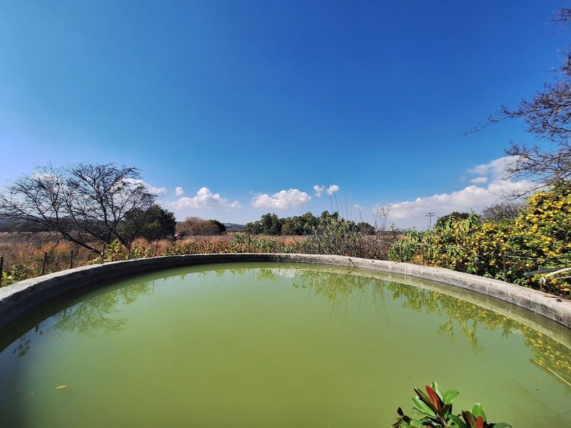 A circular concrete farm reservoir or water storage tank set against a rural landscape backdrop.