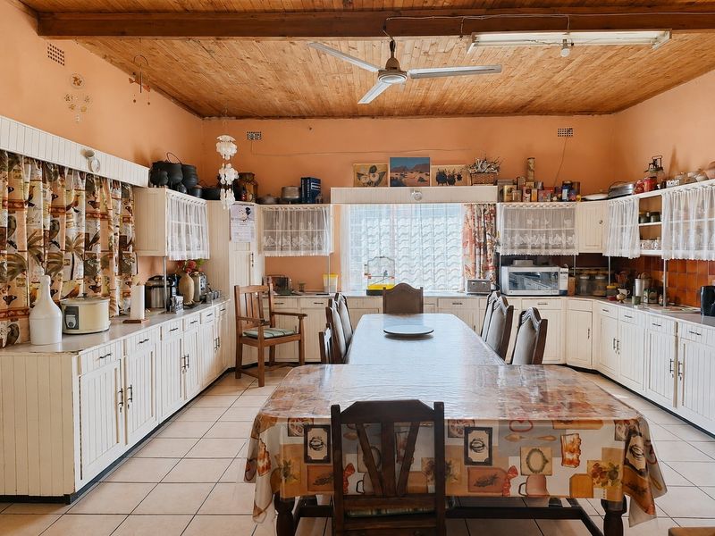 Spacious farmhouse kitchen featuring extensive built-in cabinetry, tiled flooring, and a timber-clad ceiling with a central ceiling fan.
