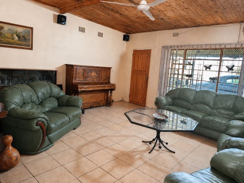 Spacious living room featuring a timber-clad vaulted ceiling, ceiling fan, and ceramic tiled flooring with large windows and security bars.