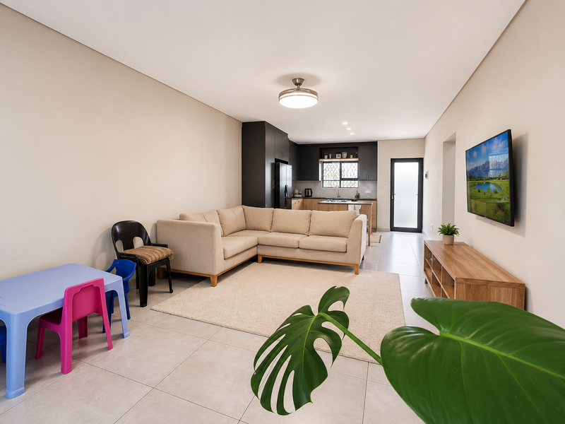 Modern open-plan living area featuring tiled floors, neutral walls, and a contemporary kitchen with dark cabinetry and integrated fixtures.