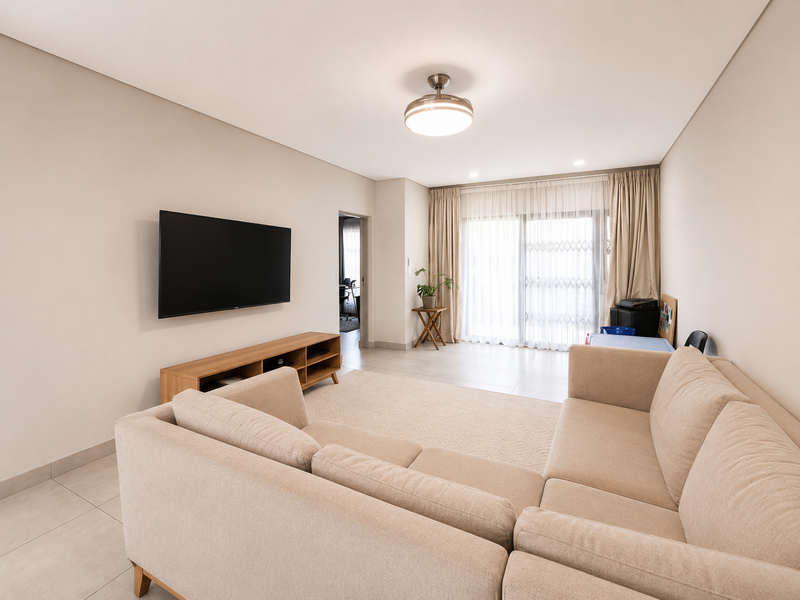 A bright and spacious living room featuring neutral tiled flooring, a modern ceiling fan, and large sliding glass doors leading to an outdoor area.