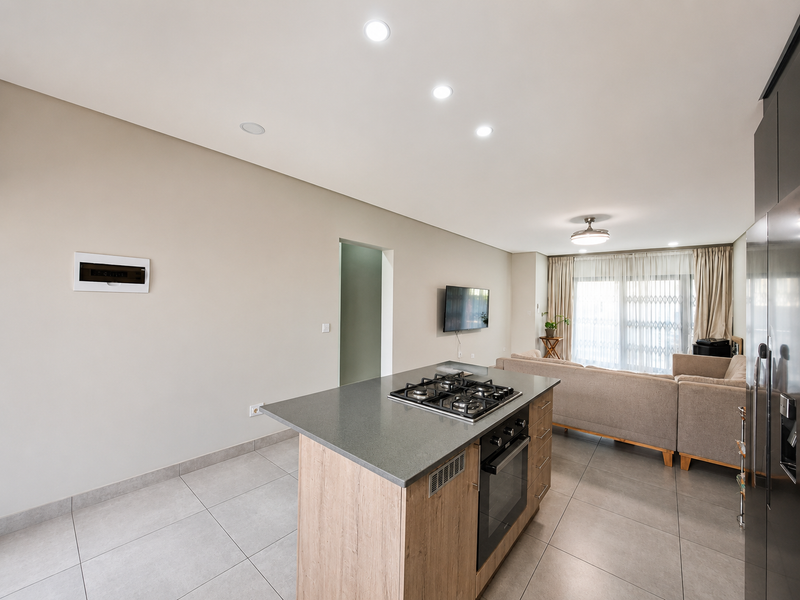 Modern open-plan living area featuring a central kitchen island with built-in gas hob and oven, flowing into a bright lounge with sliding door access.
