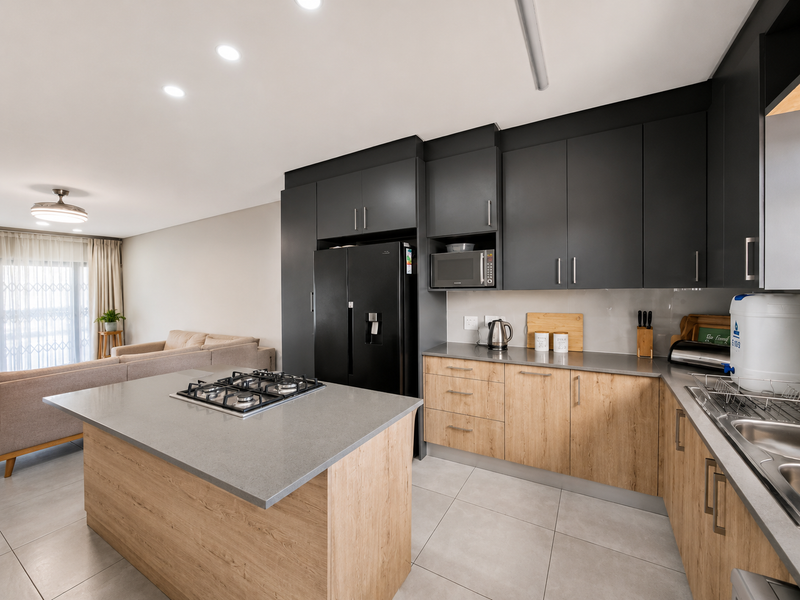 Modern open-plan kitchen featuring a central island with gas cooktop, sleek dark upper cabinetry, wood-finish lower cabinets, and stone countertops.