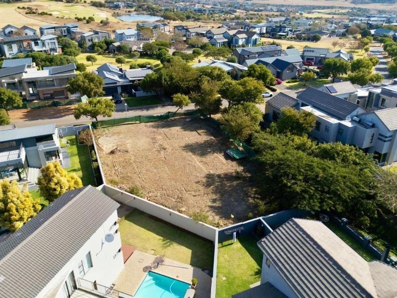 An aerial view of a vacant residential plot situated within a developed estate, surrounded by established homes and landscaping.