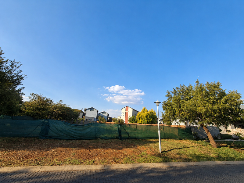 A vacant residential plot featuring a paved curb, street lighting, and perimeter fencing, situated in a developed neighborhood setting.