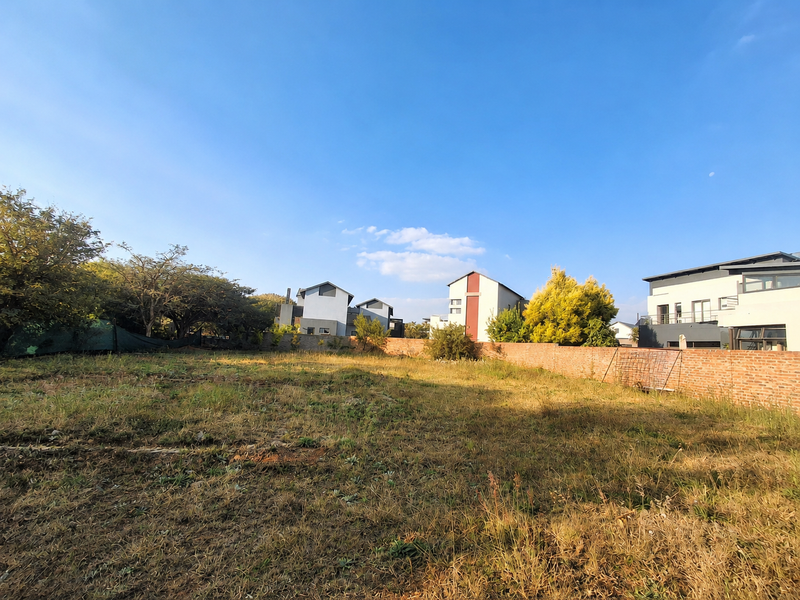 A vacant residential plot featuring a brick boundary wall and surrounding established neighborhood homes.