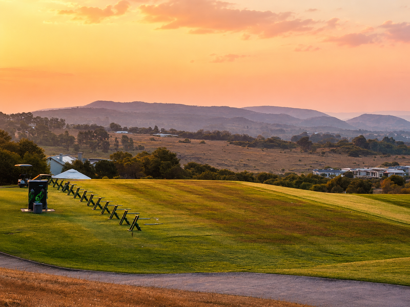 A scenic view overlooking a golf course and rolling hills at sunset, featuring a paved path and manicured green space.