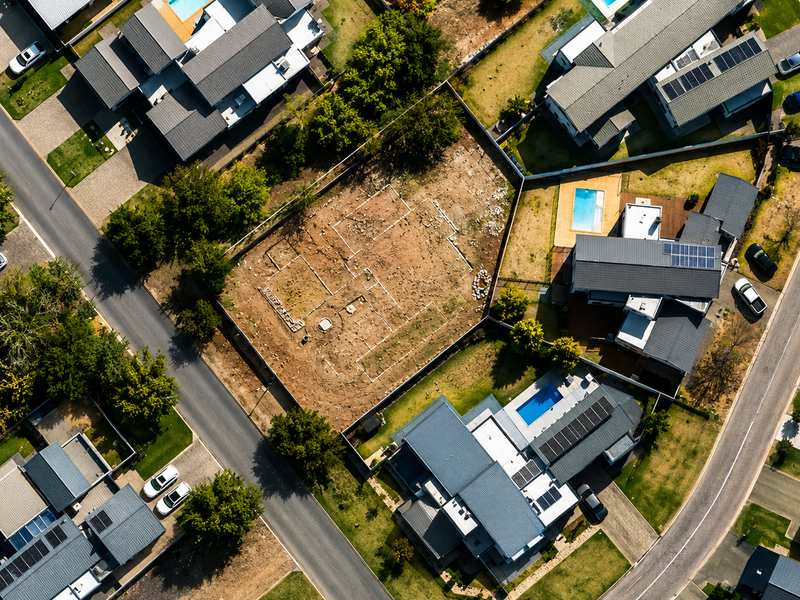 Aerial view of a vacant residential plot situated within a developed suburban estate, featuring clear boundary lines and site preparation markings.