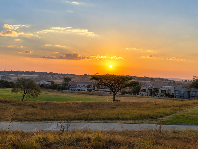 A scenic sunset view overlooking a residential estate with open grassland and a paved road in the foreground.
