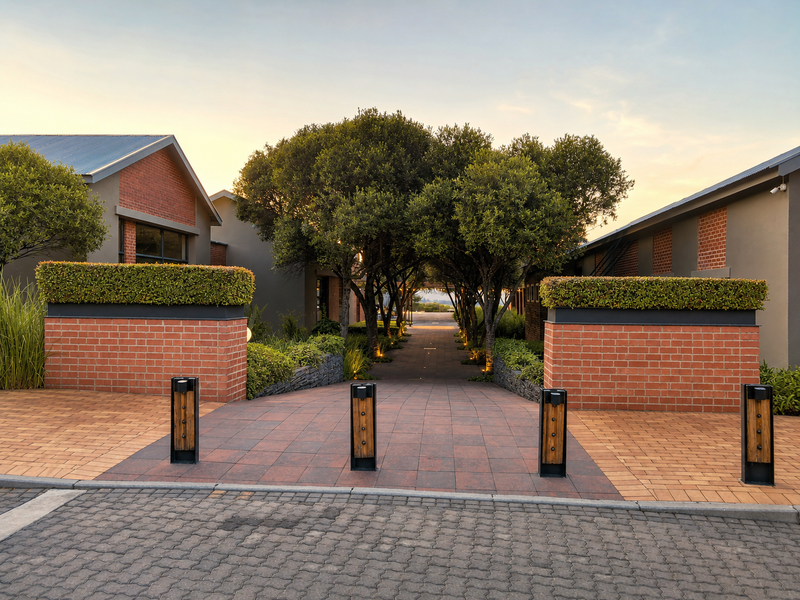 A well-maintained residential entrance featuring brick masonry pillars, paved driveway, and manicured landscaping leading towards the property.