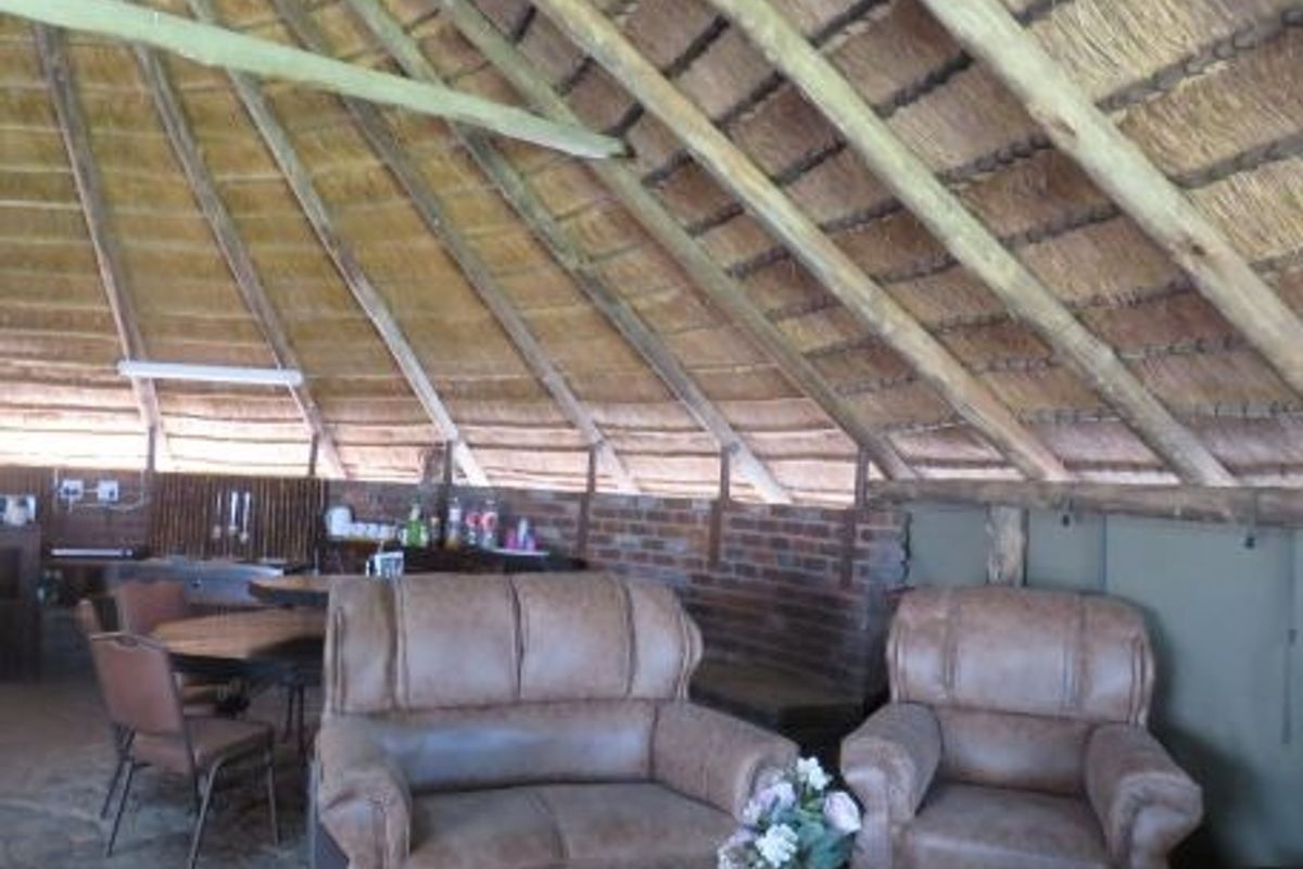 A rustic living area featuring a traditional thatched roof with exposed timber rafters, exposed brick walls, and durable stone flooring.