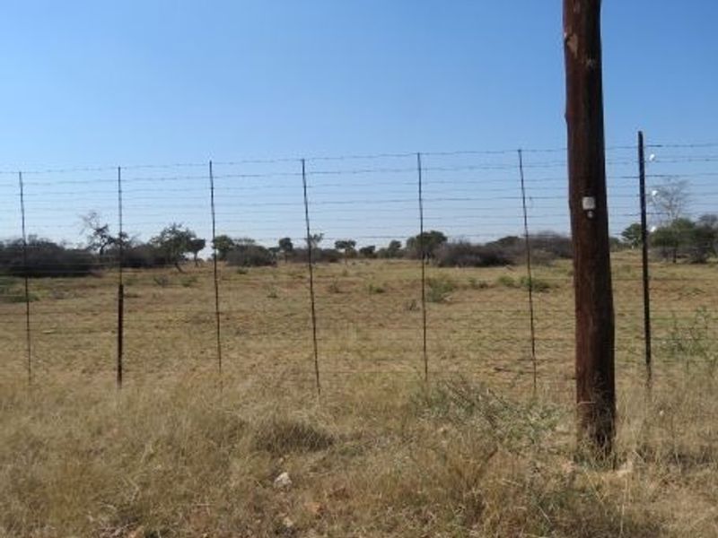 A view of the open farm land enclosed by wire fencing and wooden posts under a clear blue sky.