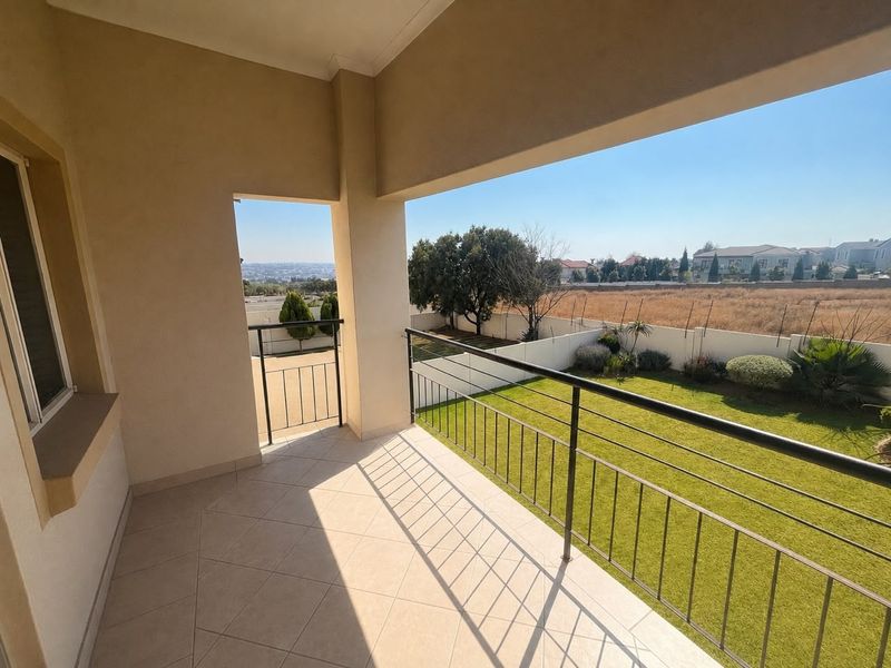 A spacious covered balcony featuring tiled flooring and a metal balustrade, offering views over the garden and surrounding neighborhood.