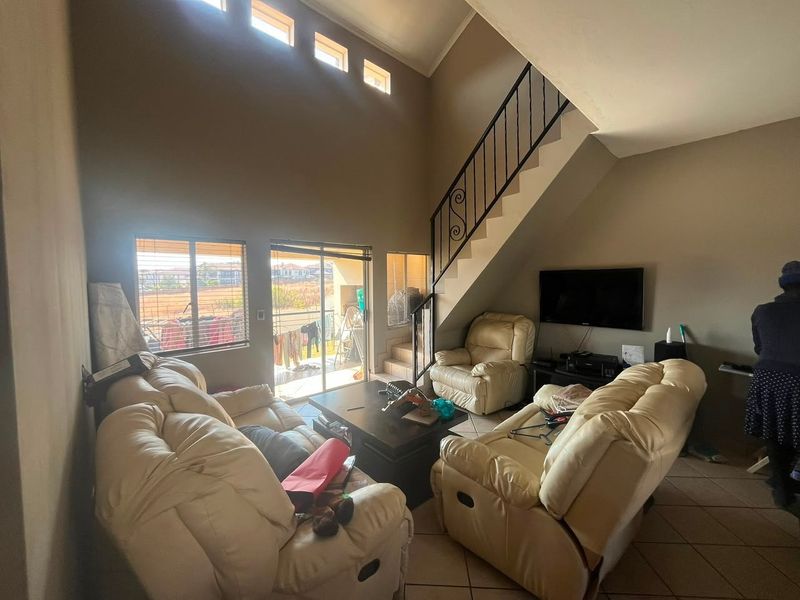 Spacious living room featuring high ceilings with clerestory windows, tiled flooring, and an internal staircase with a decorative wrought iron balustrade.