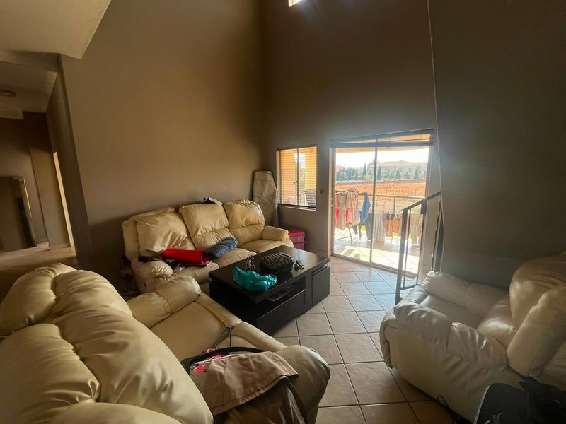 Spacious living room featuring double volume ceilings, tiled flooring, and direct access to a balcony through sliding glass doors.
