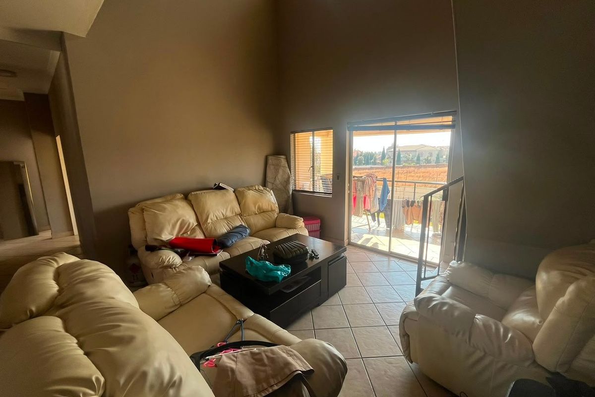 Spacious living room featuring double volume ceilings, tiled flooring, and direct access to a balcony through sliding glass doors.