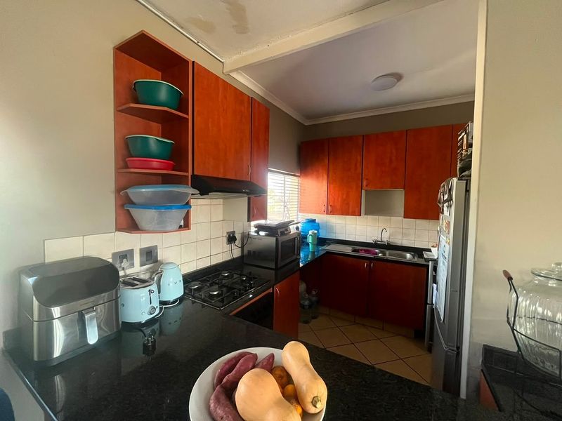 A functional kitchen featuring dark granite countertops, wooden cabinetry, a gas hob with extractor fan, and a double sink with tiled backsplash.