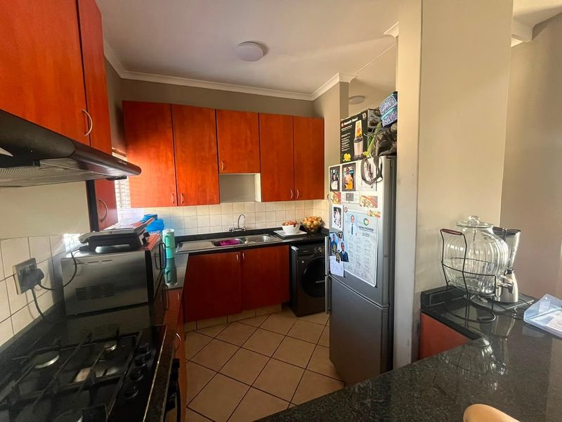 Functional kitchen featuring warm-toned wooden cabinetry, granite countertops, a gas hob with extractor, and tiled flooring with a practical layout.