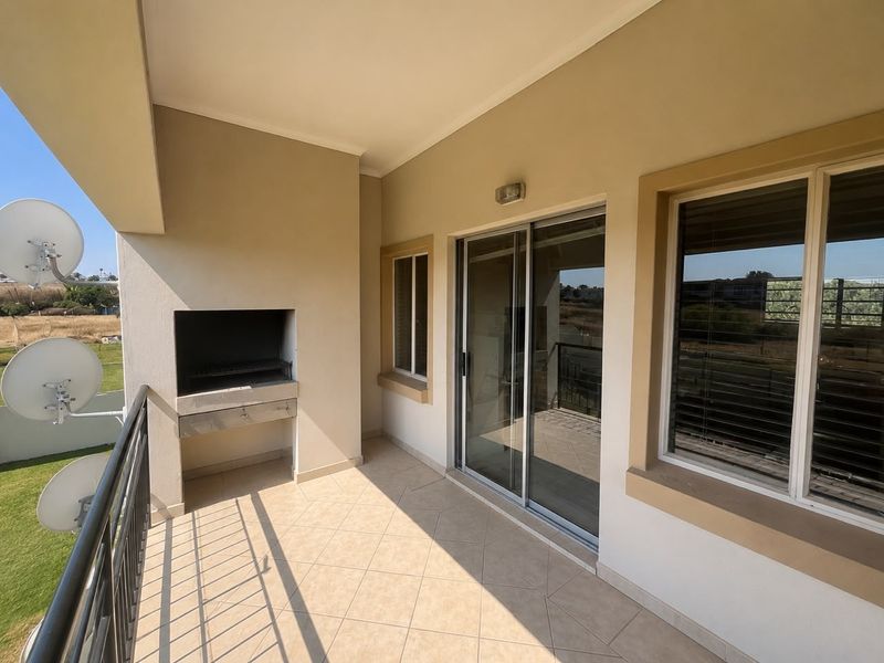 A covered balcony featuring tiled flooring, a built-in braai, and a sliding glass door providing access to the interior.