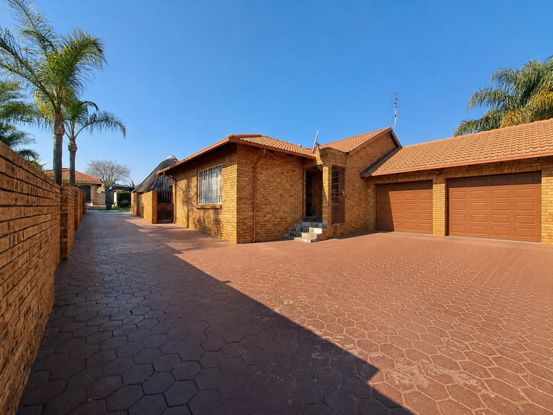 A well-maintained face-brick house featuring a double garage, paved driveway, and secure boundary wall, presenting a neat and classic exterior facade.