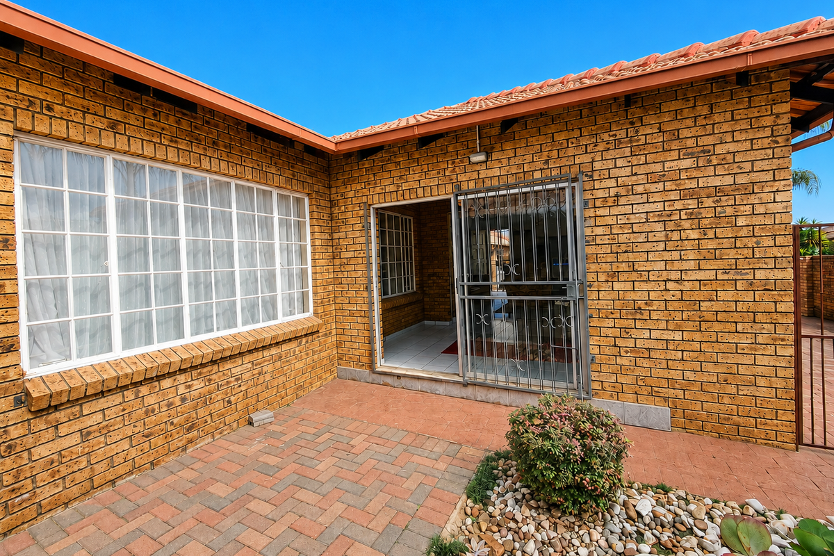A rear exterior view featuring a face brick facade, tiled roof, paved patio area, and a secure sliding door entrance.