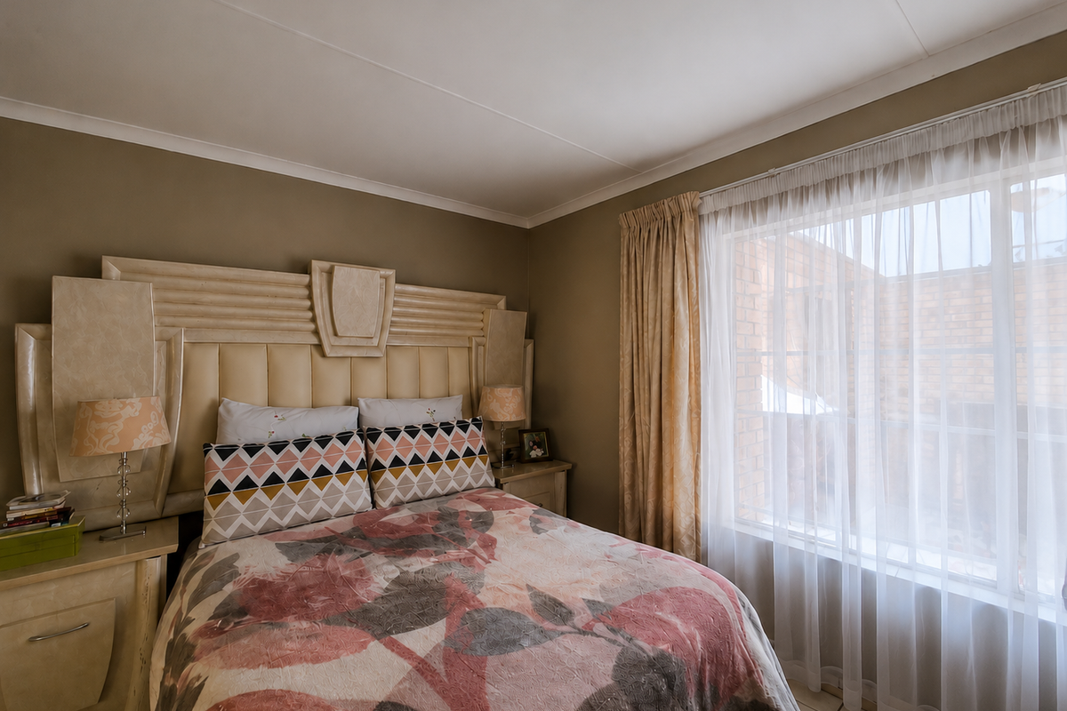 A bedroom featuring a built-in headboard and matching bedside tables, with natural light entering through a window dressed with curtains.