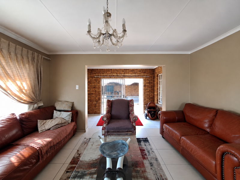 Spacious living room featuring neutral walls, tiled flooring, and an exposed brick feature wall leading to an outdoor area through a sliding glass door.