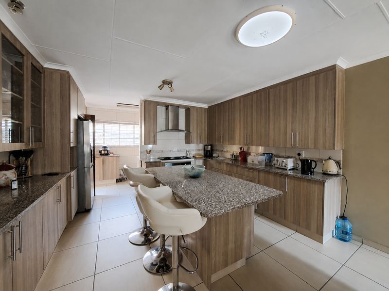 A well-maintained kitchen featuring wood-finish cabinetry, granite countertops, a central island, and integrated stainless steel appliances with tiled flooring throughout.