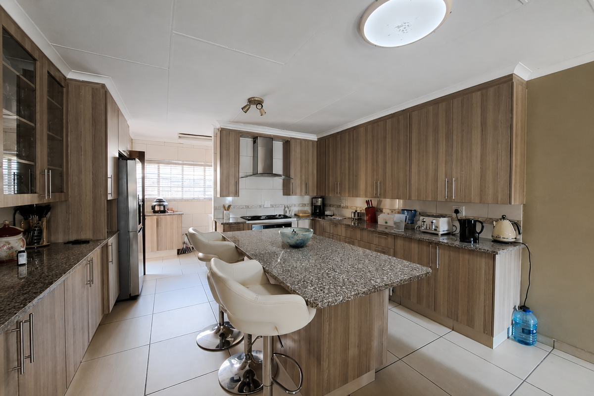 A well-maintained kitchen featuring wood-finish cabinetry, granite countertops, a central island, and integrated stainless steel appliances with tiled flooring throughout.