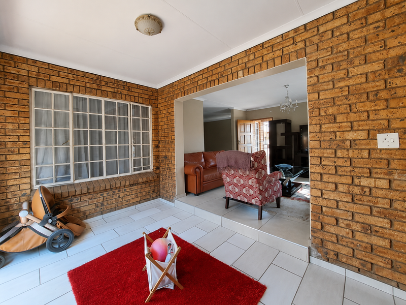 A living area featuring exposed brick walls, tiled flooring, and a large window, with an open-plan transition to an adjacent lounge space.