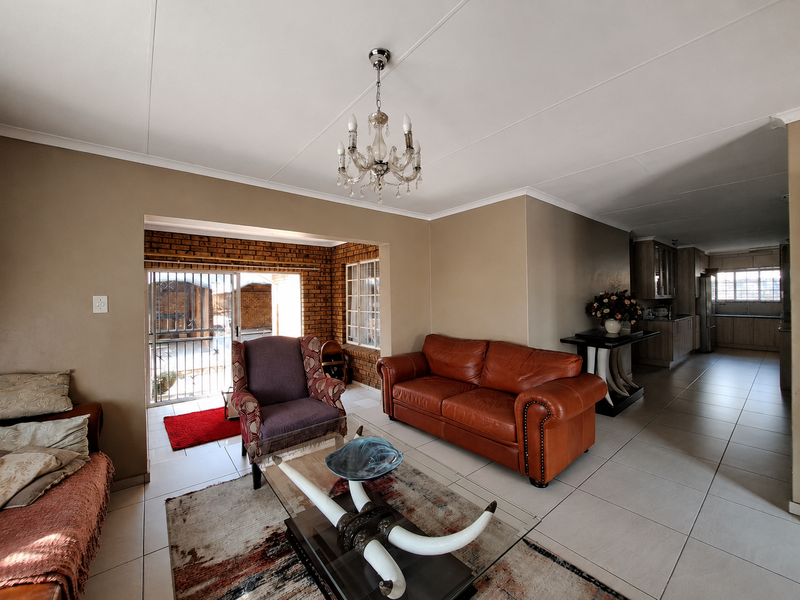 Spacious open-plan living area featuring tiled floors, an exposed brick accent wall, and a seamless transition to the kitchen and outdoor patio space.