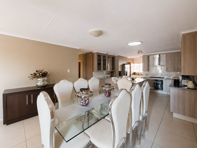 Spacious open-plan dining and kitchen area featuring modern built-in cabinetry, granite countertops, integrated appliances, and tiled flooring throughout.