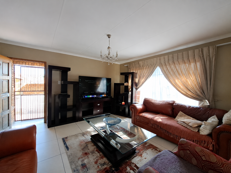 A comfortable living room featuring tiled flooring, a central chandelier, and direct access to an exterior security gate.