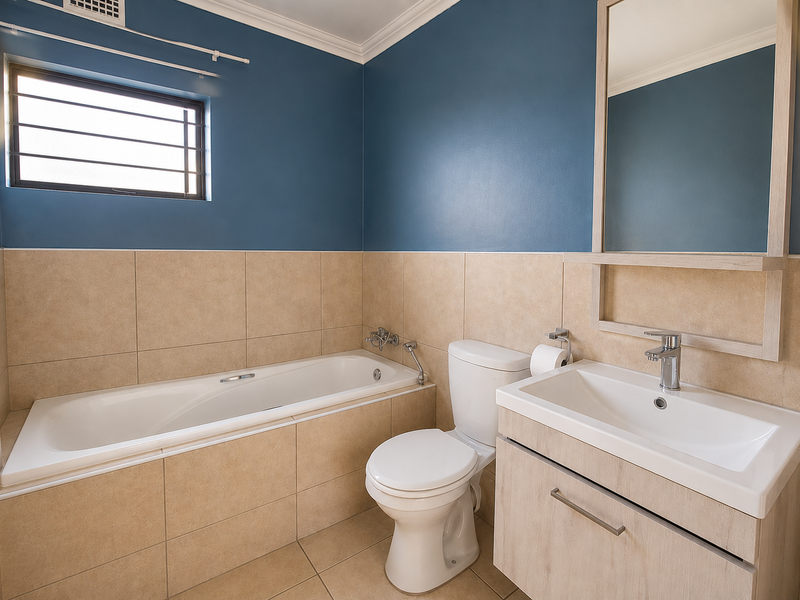 A clean, well-maintained bathroom featuring a built-in bathtub, modern vanity with basin, and neutral wall tiling with blue accent paint.