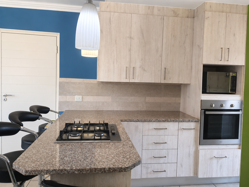 Modern kitchen featuring light wood-grain cabinetry, stone-look countertops, a built-in gas hob, oven, and microwave, complemented by a neutral tiled backsplash.
