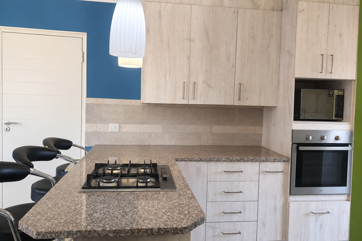 Modern kitchen featuring light wood-grain cabinetry, stone-look countertops, a built-in gas hob, oven, and microwave, complemented by a neutral tiled backsplash.