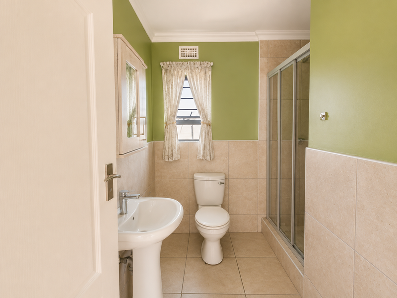 A clean and functional bathroom featuring a pedestal basin, toilet, and a glass-enclosed shower with neutral wall and floor tiling.