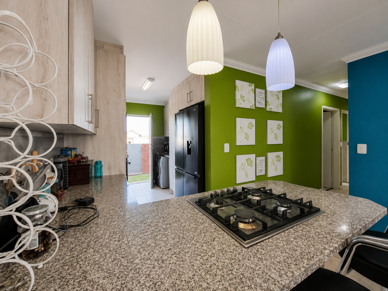 Modern kitchen featuring granite countertops, a built-in gas hob, and ample cabinetry, with an adjacent laundry area and vibrant accent walls.
