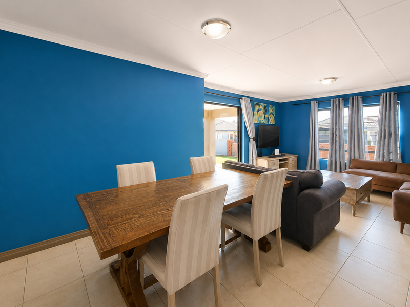Open-plan living and dining area featuring tiled flooring, bright blue accent walls, and direct access to an outdoor patio through sliding glass doors.