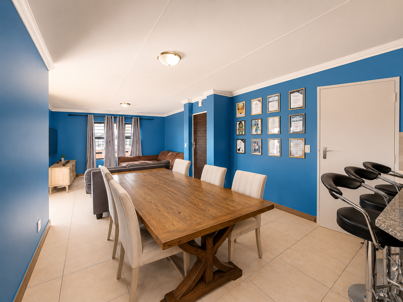 An open-plan living and dining area featuring tiled flooring, crown molding, and vibrant blue walls, creating a functional and connected living space.