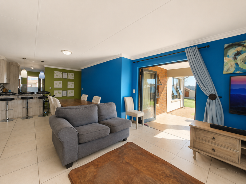 Open-plan living and dining area featuring tiled floors, a breakfast bar, and seamless access to an outdoor patio through large bi-fold doors.
