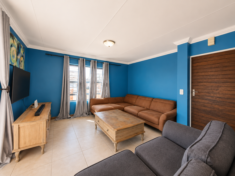 A bright living room featuring tiled flooring, blue accent walls, and a horizontal slat timber door, providing a functional and well-maintained living space.