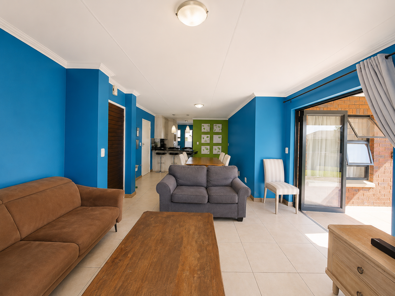 Open plan living and dining area featuring tiled floors, vibrant blue walls, and direct access to an outdoor patio through a large sliding glass door.